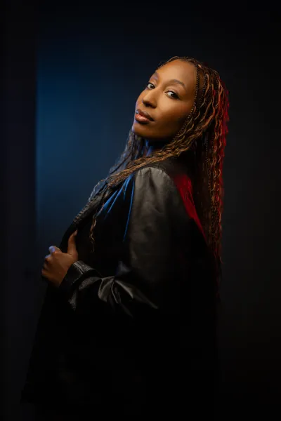Mid-torso level headshot of a woman with red and blue light on opposite sides of her